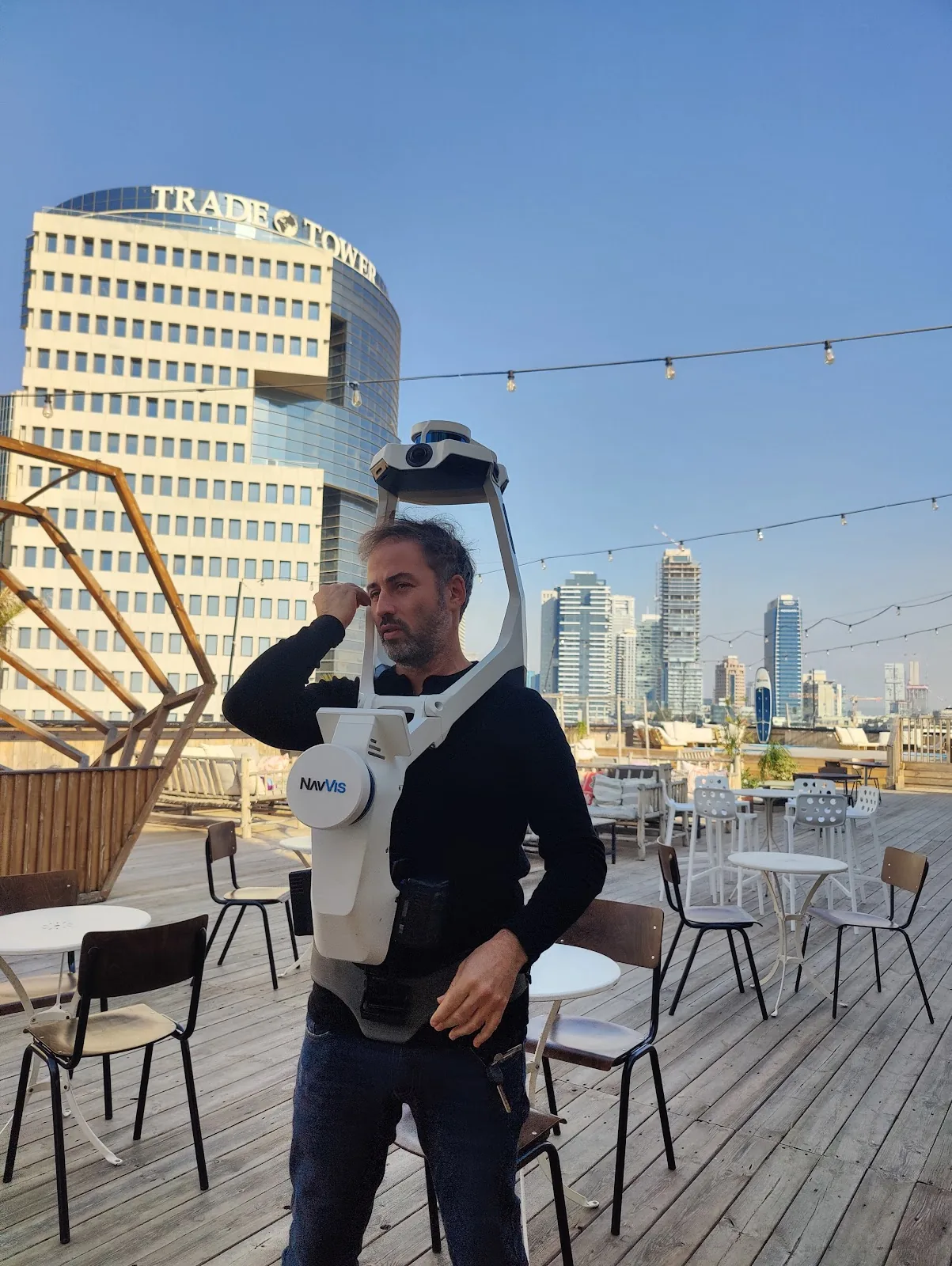 עודד מקובקי עם סורק לייזר נייד על גג מול קו הרקיע של תל אביב